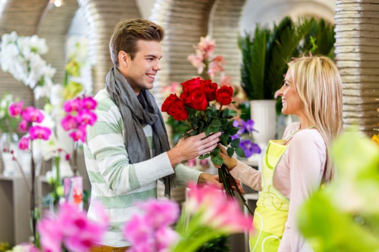 Young man buying red roses in a flower shop.